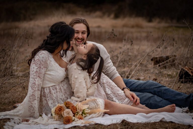 mother, father, and child holding each other in long grass field by elk lake for maternity family photoshoot victoria bc with alyssa orrego photography