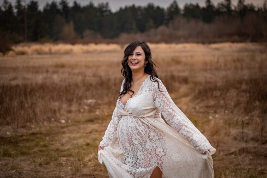 pregnant mom in ivory flowy dress in long grass field by elk lake for maternity photoshoot victoria bc with alyssa orrego photography