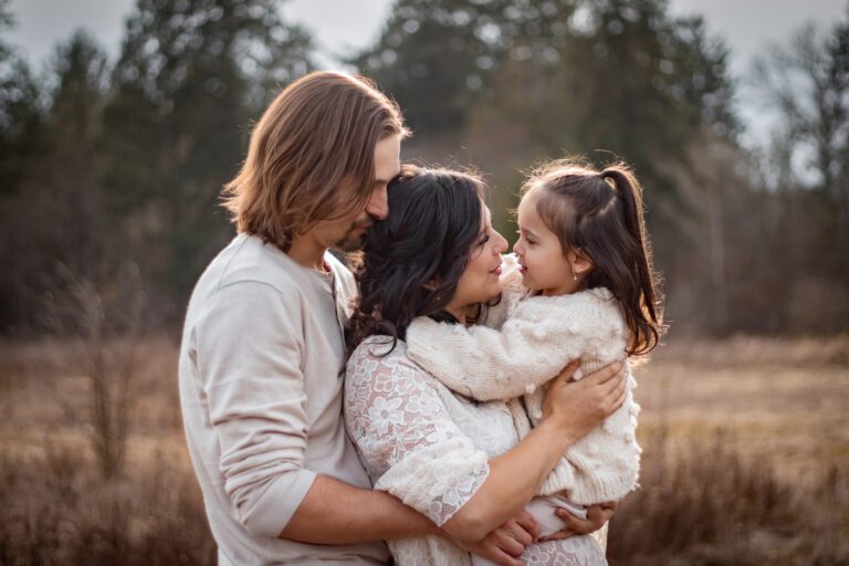 mother, father, and child holding each other in long grass field by elk lake for a lifestyle family photography session victoria bc with alyssa orrego photography