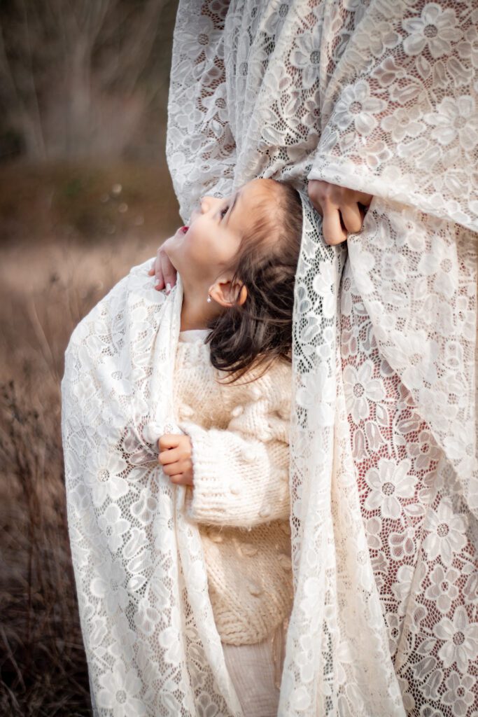 child and pregnant mom in ivory flowy dress playing in long grass field by elk lake for maternity photoshoot victoria bc with alyssa orrego photography