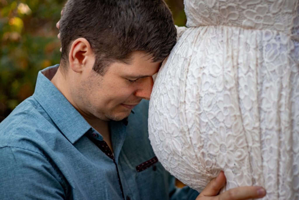 romantic couple man kissing belly in ivory flowy dress in forest by horth hill for maternity photoshoot victoria bc with alyssa orrego photography